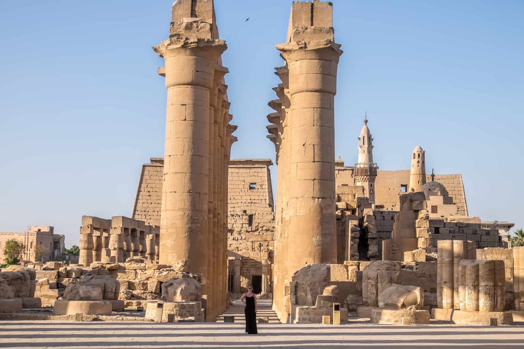 A woman stands in between two towering rows of golden columns of Luxor Temple in Egypt