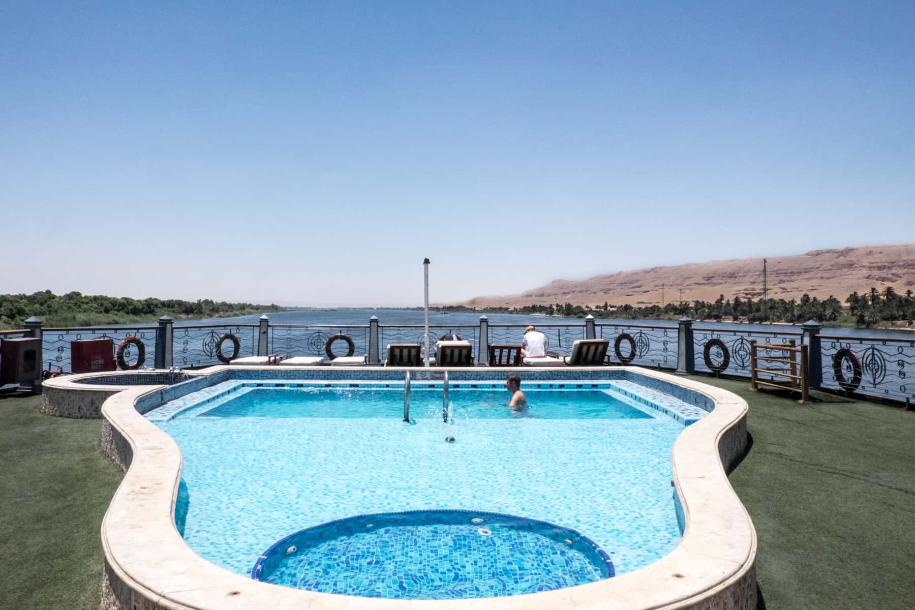 A swimming pool on the top deck of a Nile cruise boat in Egypt, with the Nile River rock formations in the background