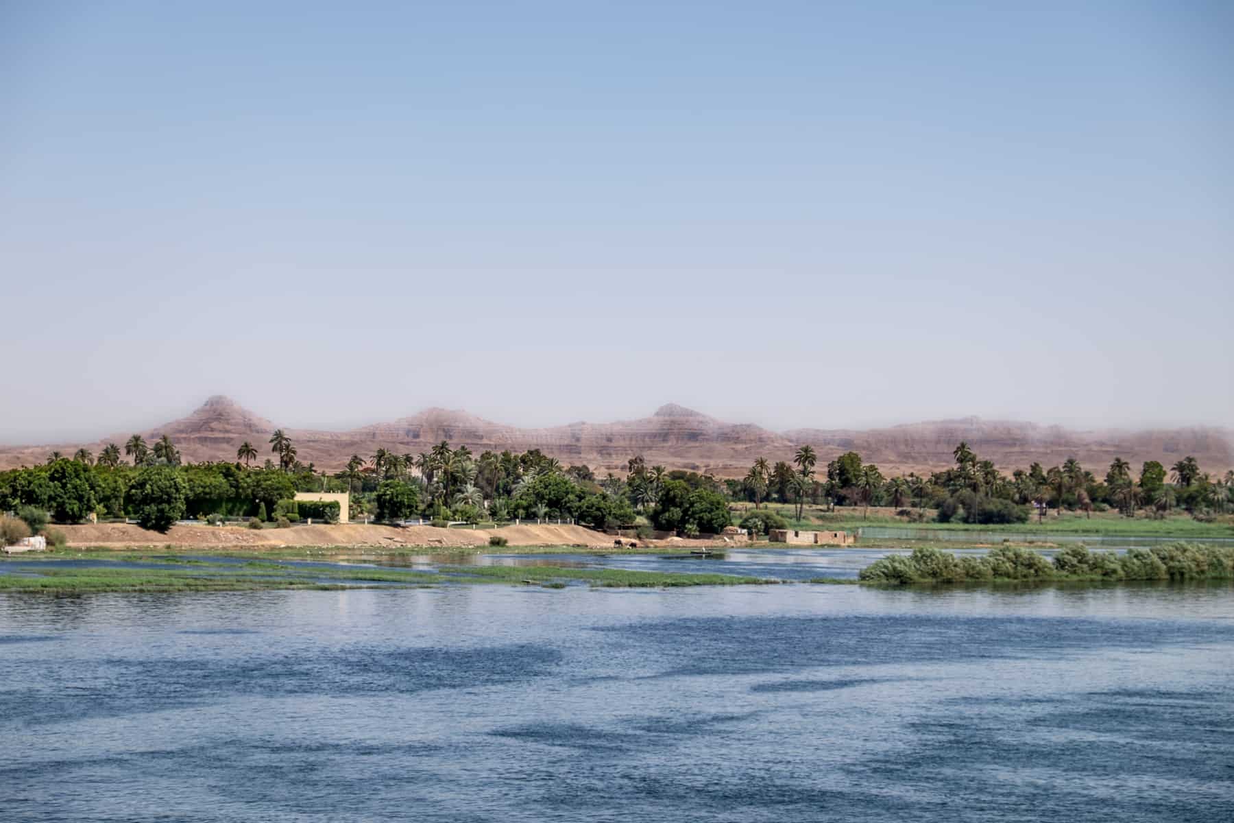 Views of the desert lands and pockets of oasis that line the Nile, backed by mountains, as seen on a Nile Cruise between Aswan and Luxor