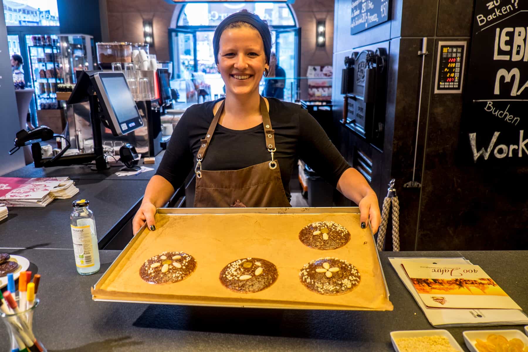 Four gingerbread cookies are placed on a large baking tray ready for the oven, held by a woman leading the gingerbread baking class in Nuremberg