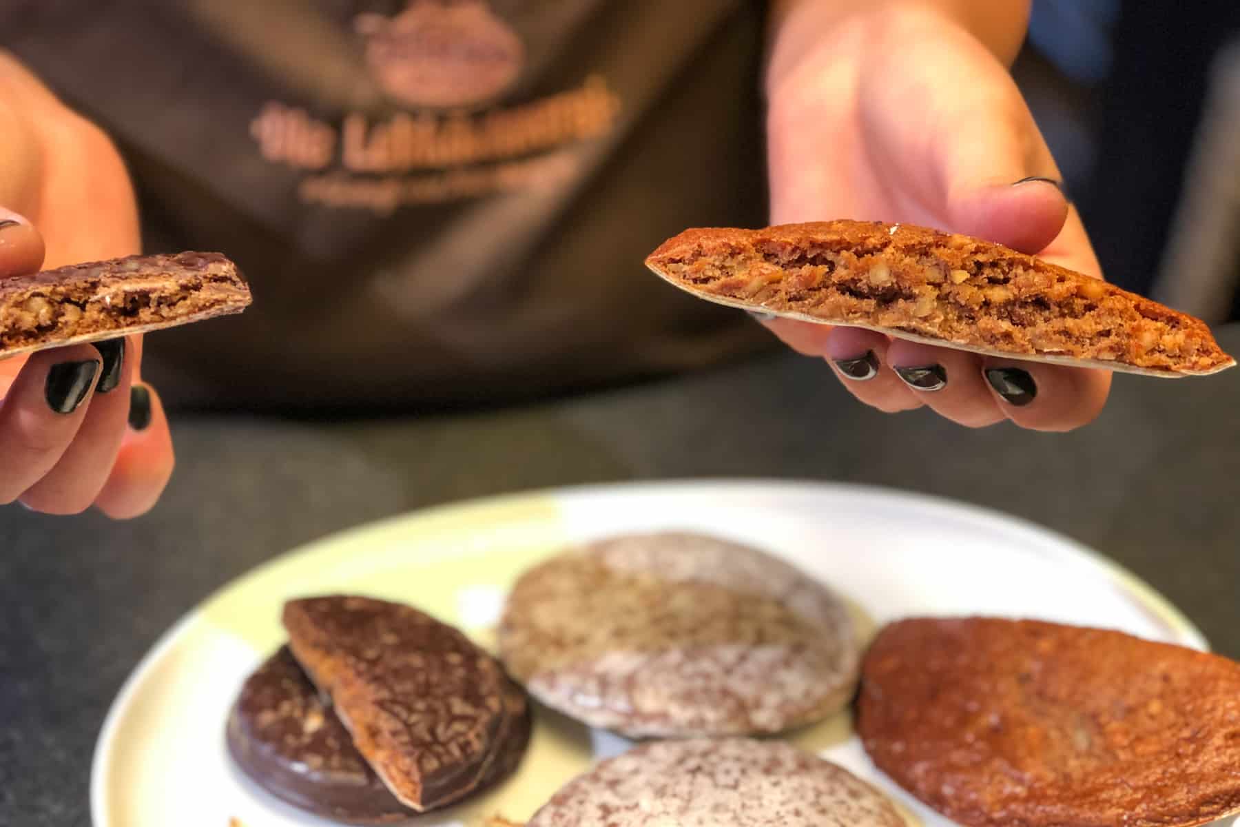 Un par de manos sostiene un pan de jengibre de Nuremberg partido por la mitad para mostrar la mezcla de nueces en el interior y cómo se hace