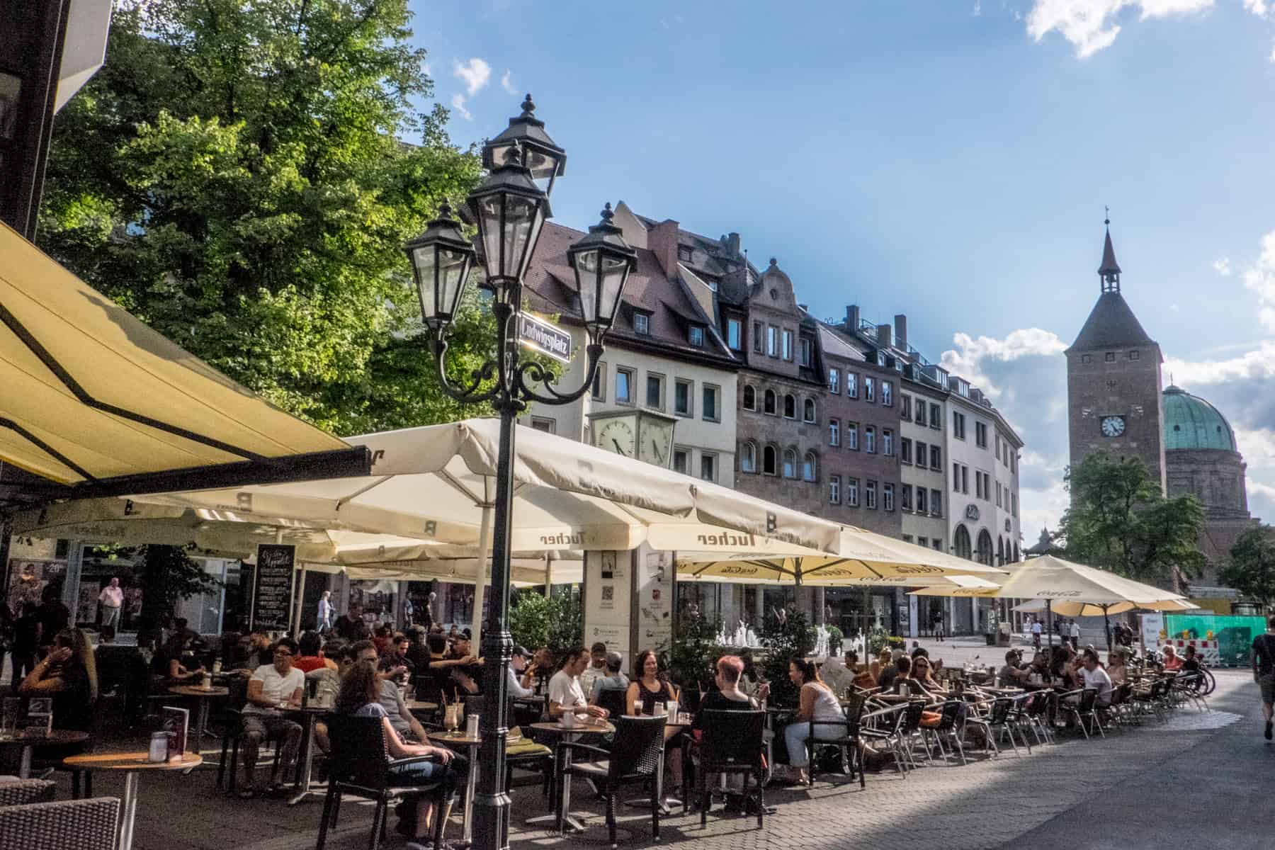 A long line of al fresco dining tables under yellow umbrellas sit within a square in Nuremberg Old Town