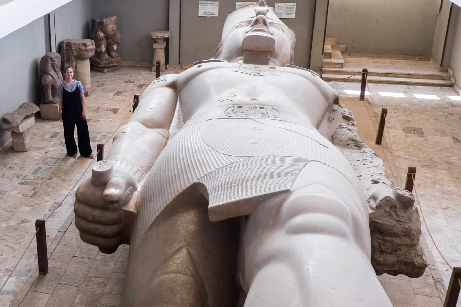 A woman stands beside the colossal Ramesses statue which lays on the floor at the museum in Memphis Egypt