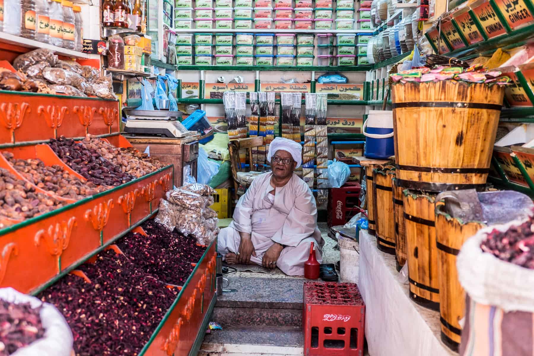 Mr Abed, dressed in a white tunic and headdress, sitting in the middle of his spice shop in Aswan's Sharia el Souk