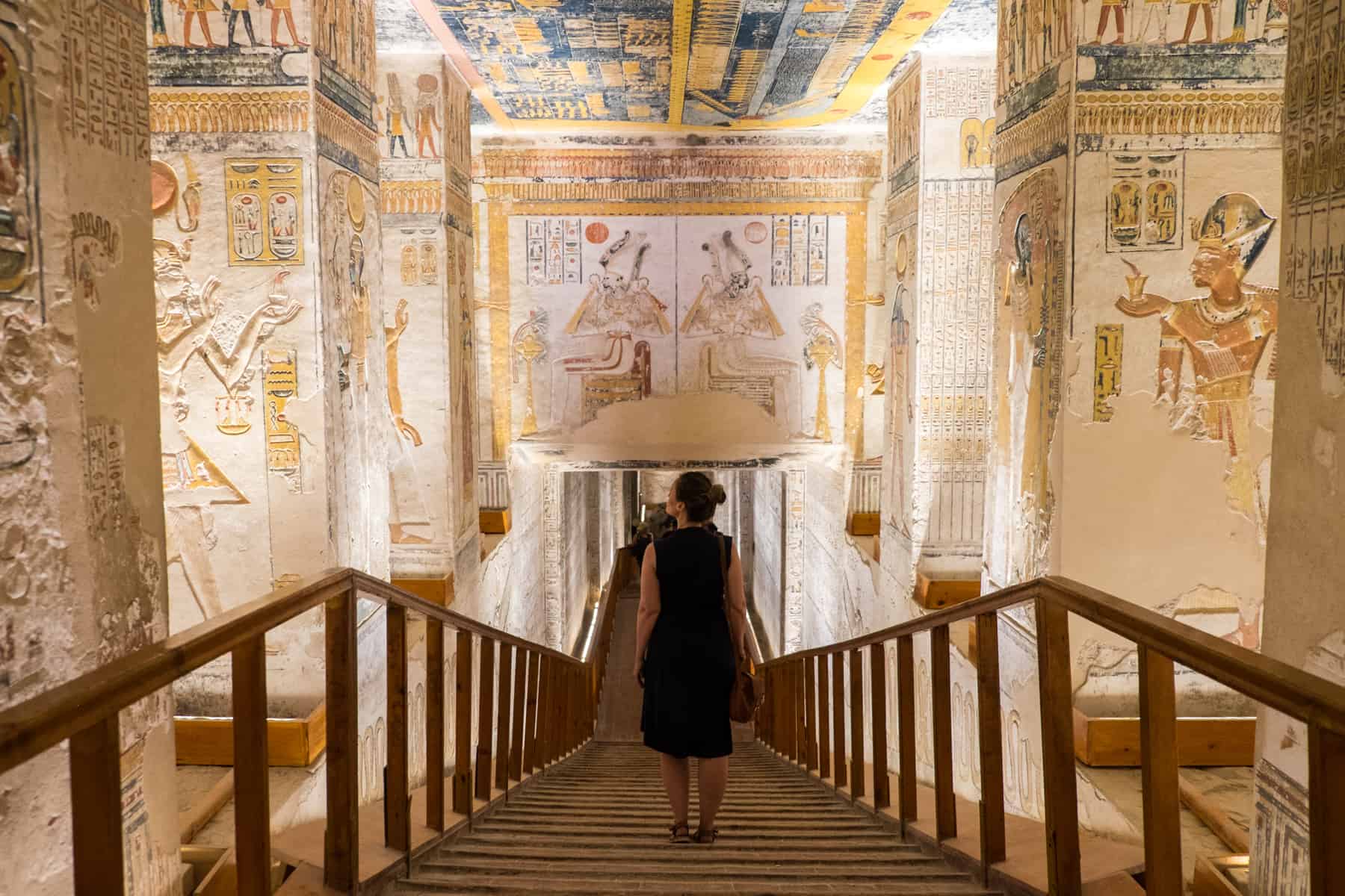 A woman walks down a wooden platform inside a tomb in the Valley of the Kings in Egypt, where every wall space and ceiling is filled with scripture and images