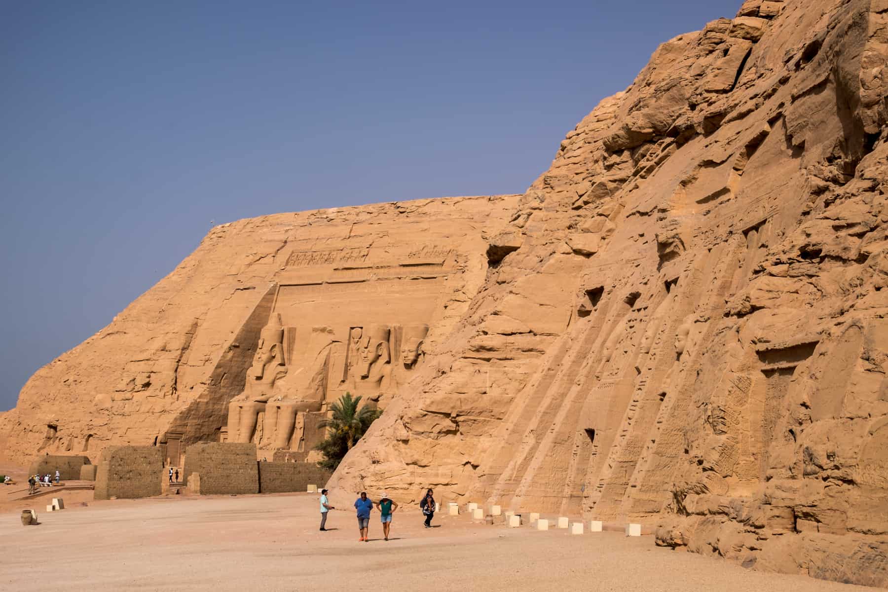 A wide shot of both mountain carved temples of Abu Simbel in Egypt, with statues and scripture carved into ochre mountain rocks