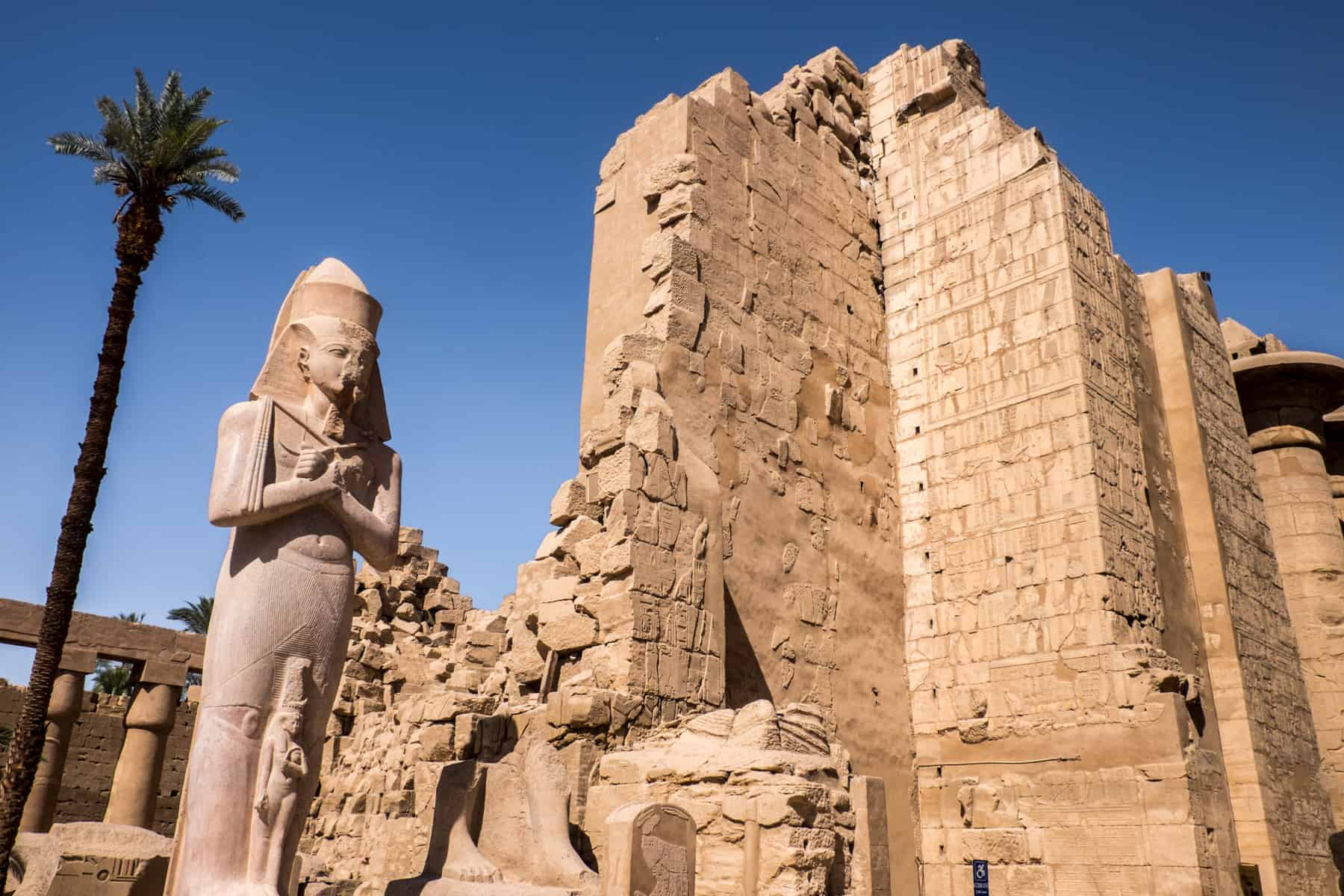 A statue and tall, crumbling stone brick walls mark on of the man entrances to the large, multi-complex structure of Karnak Temple in Luxor, Egypt