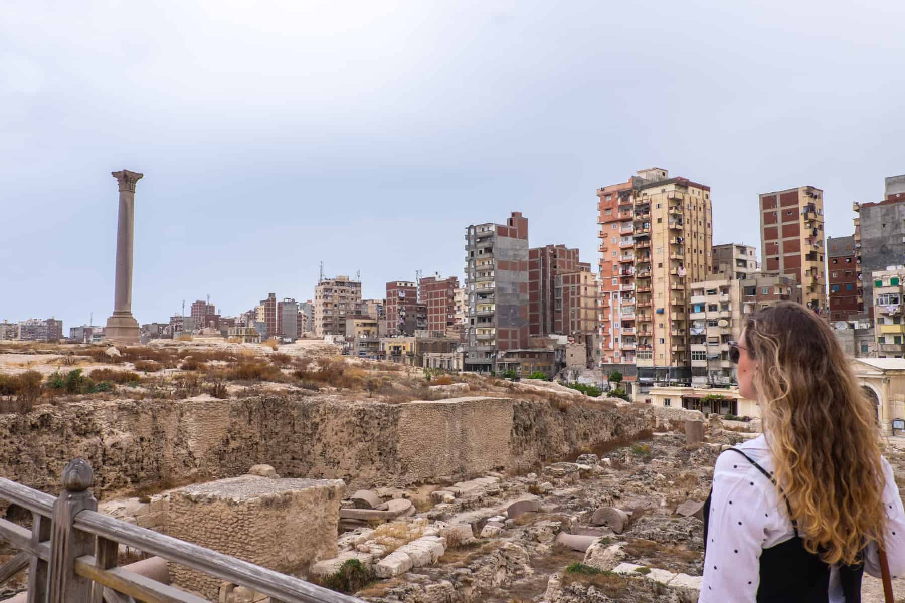 A woman stands overlooking the archaelogical site of Pompey's Pillar in Alexandria, Egypt which is surrounded by modern apartment buildings