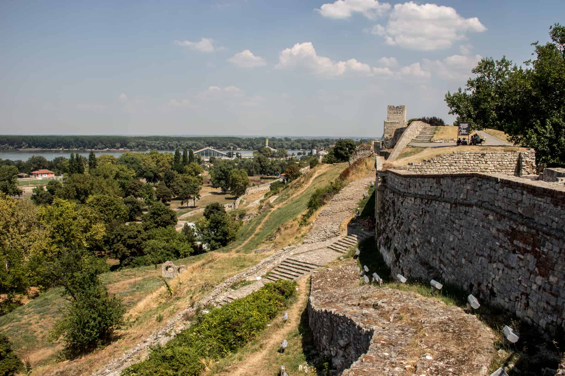 Stone walls and staircases of the hilltop Belgrade Fortress, overlooking a forested area next to a River. 