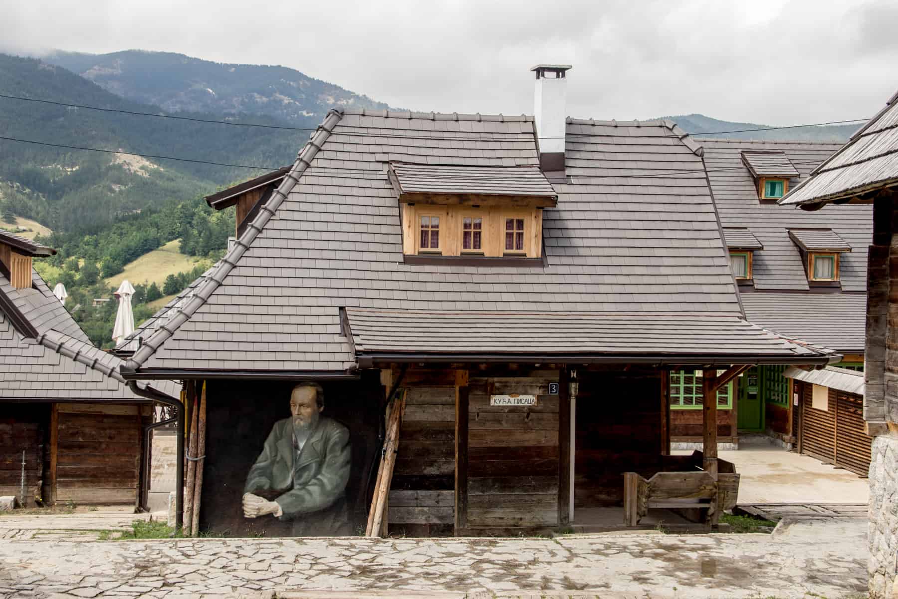 A painting of a man of a building made of wood with a huge grey roof with windows. 