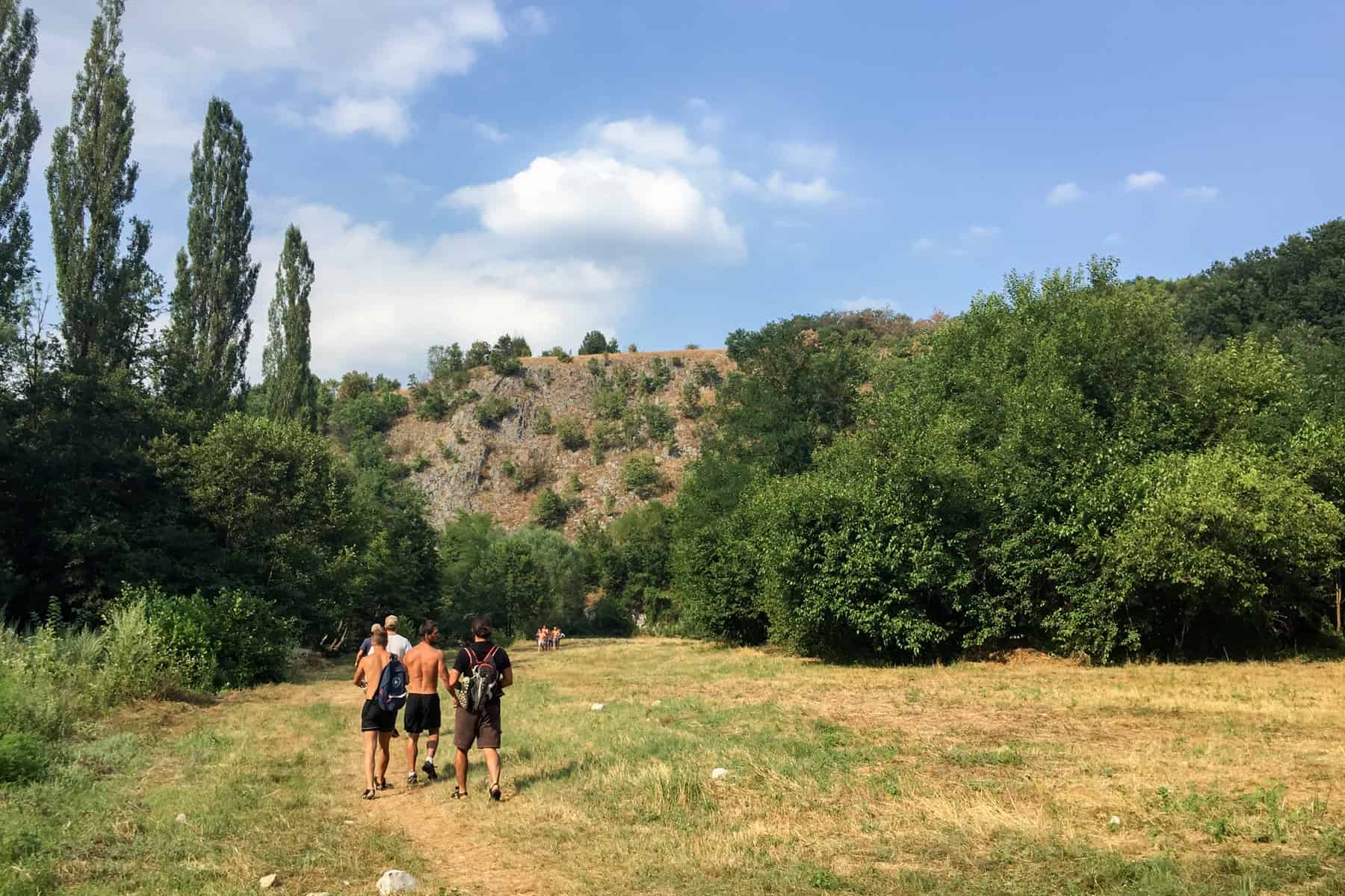 Two groups of people walking through the open area of a forested gorge. Tree dotted rock mounds can be seen in the distance. 