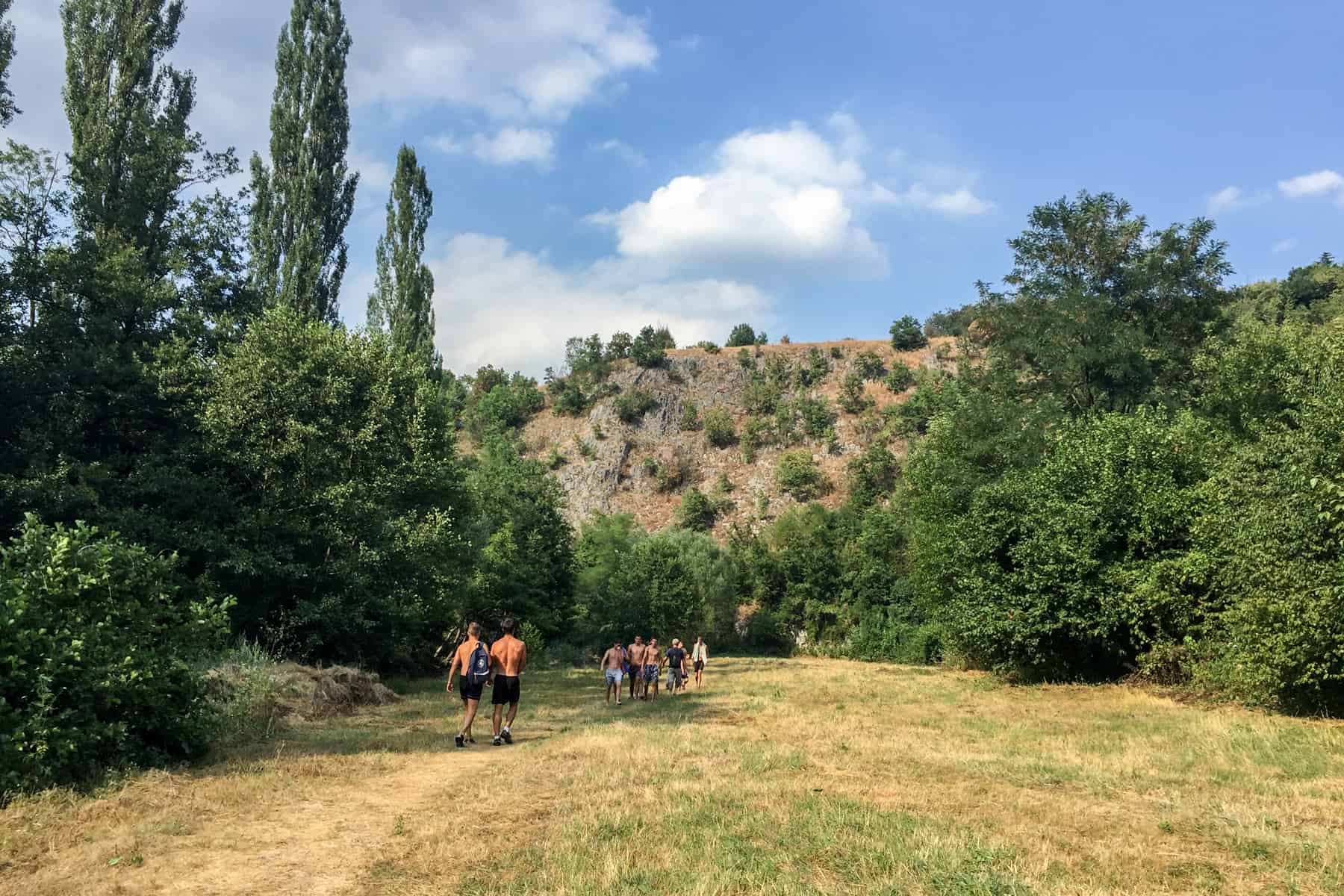 Two groups of people walking through the open area of a forested gorge. Tree dotted rock mounds can be seen in the distance. 