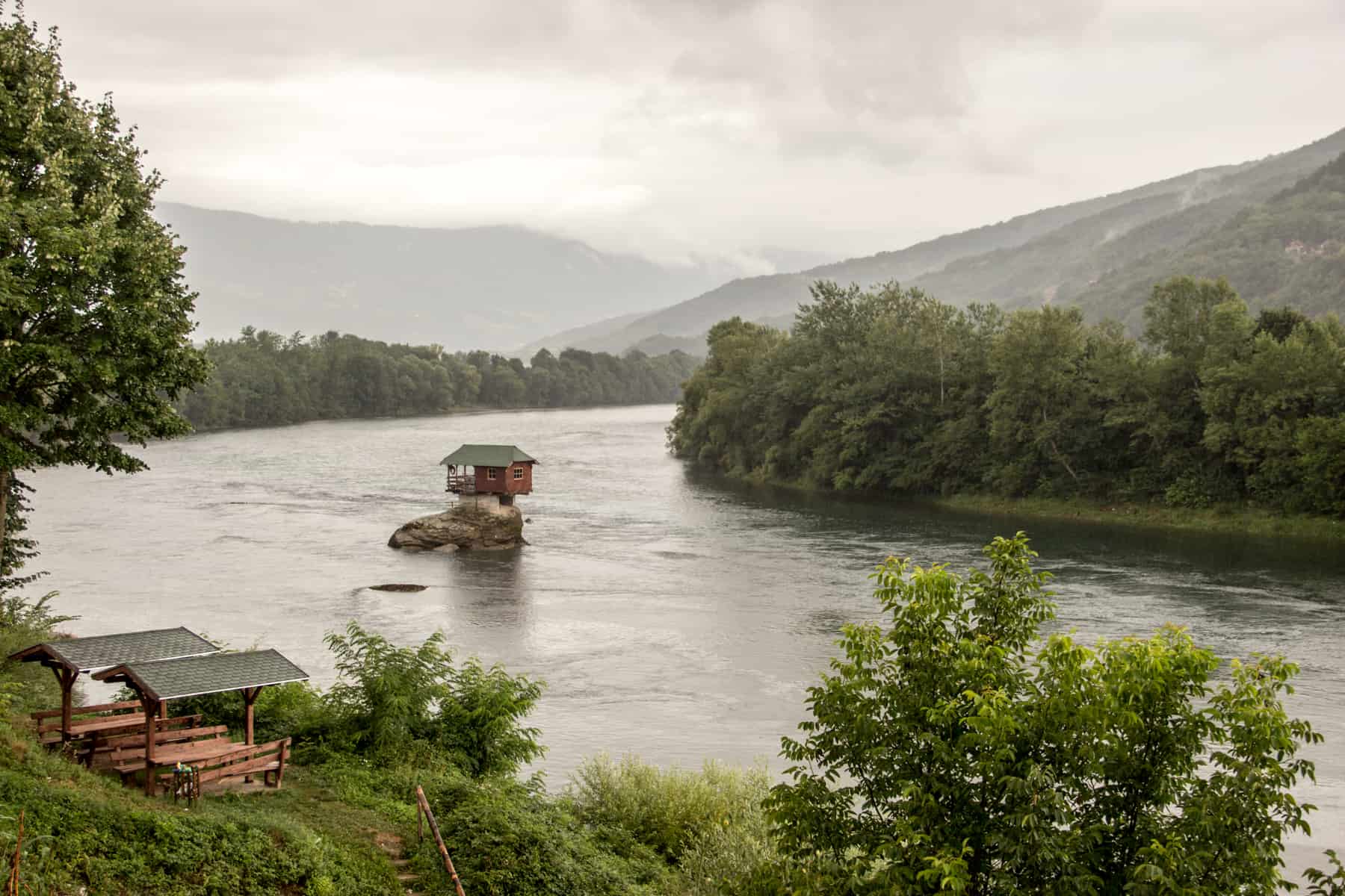 A tiny House on the River Drina in Serbia, perched on a rock in the middle of the water, surrounded by forest. 