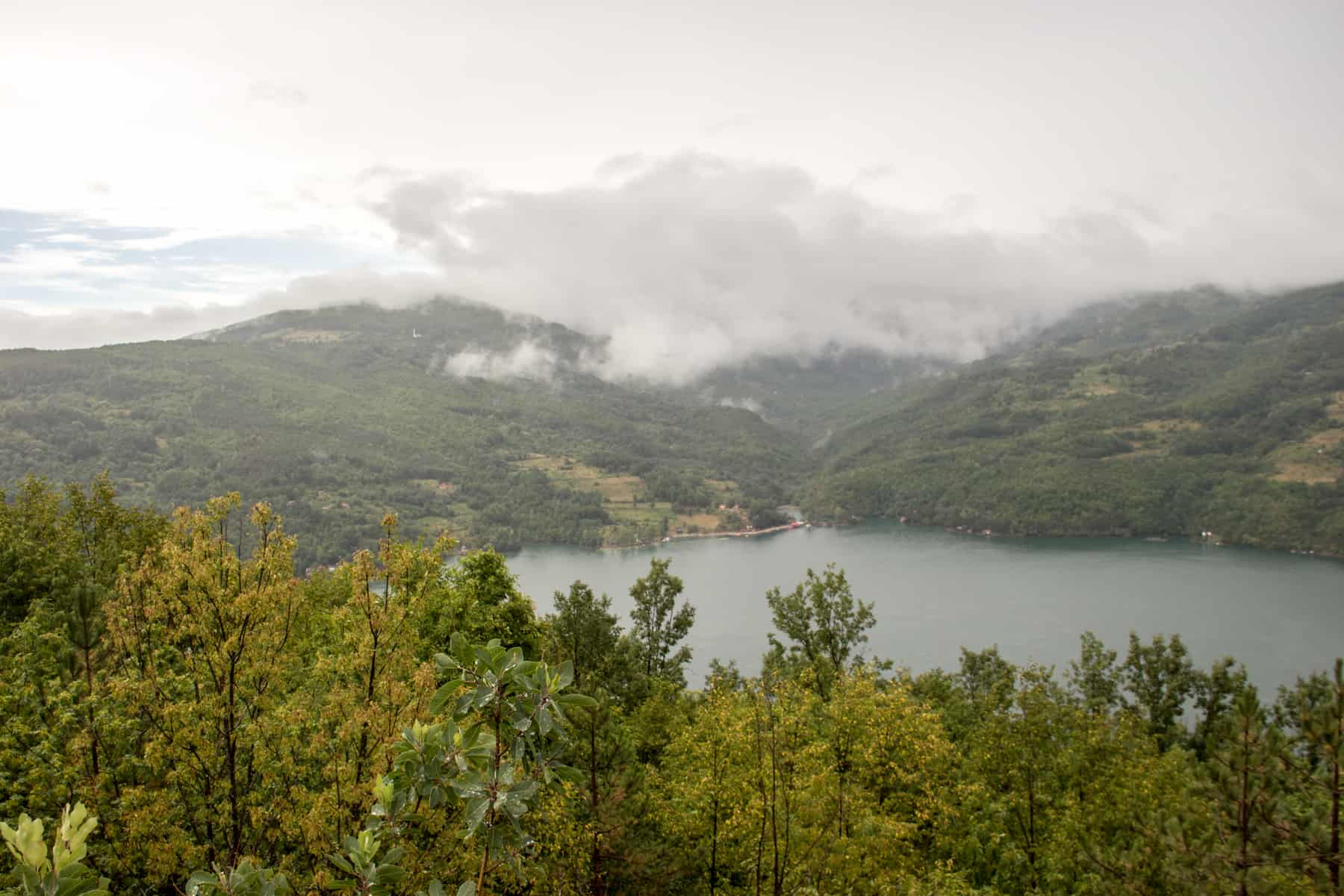 Mist rises over a lake surrounded by rolling hills covered in thick forest. 