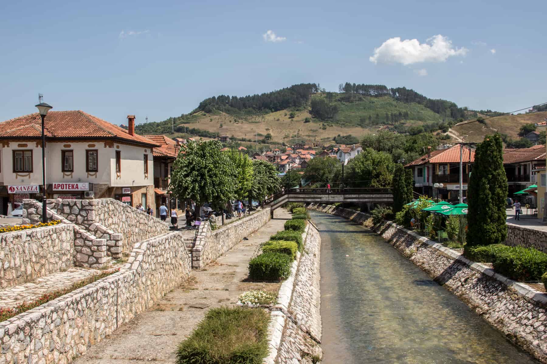 View from a white stone-walled river, looking towards a village in the hills made up of white houses with orange rooftops. 