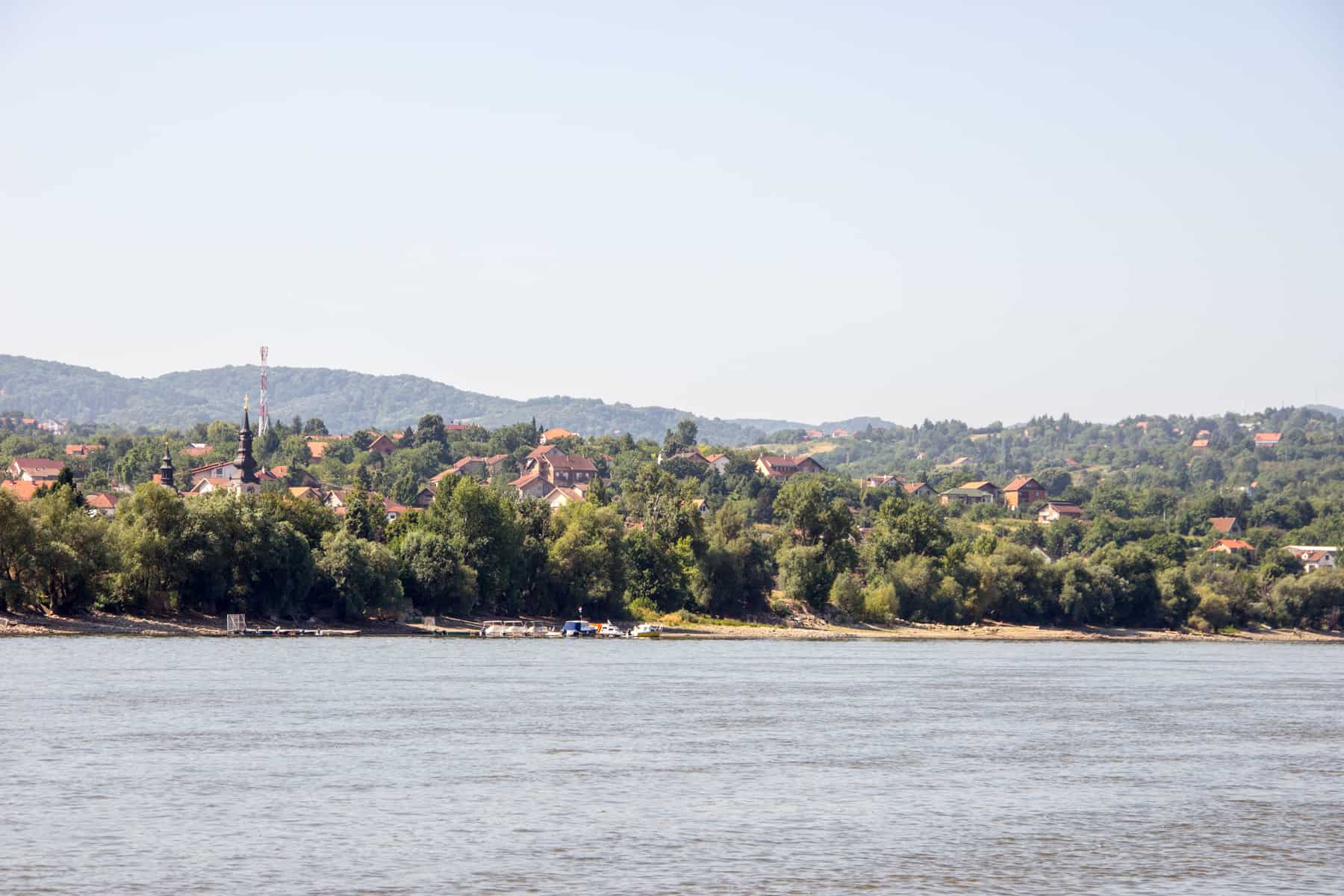 Orange red houses poke through thick forest on the banks of the Danube River in Serbia. 