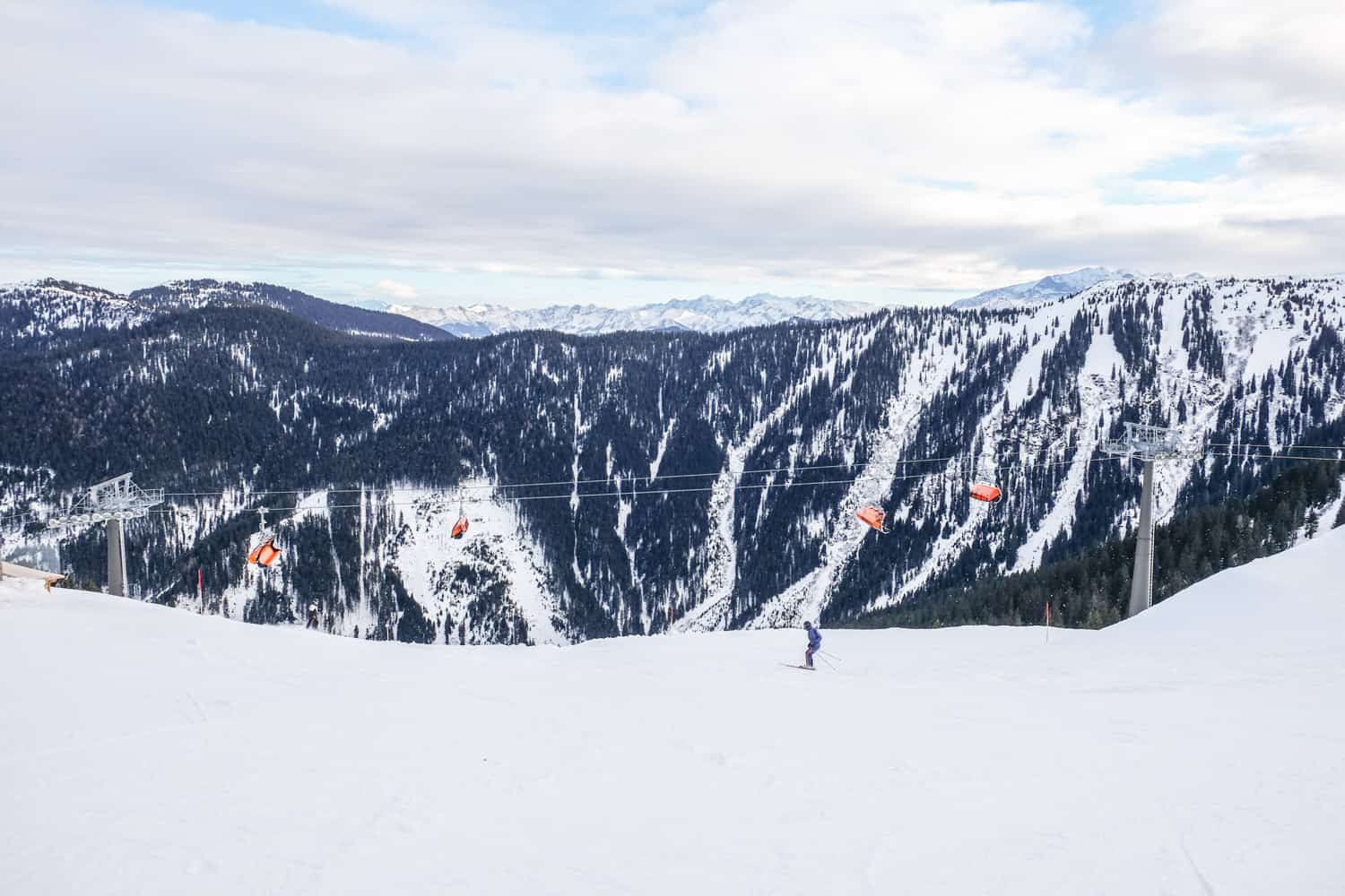 A single skier on a bowl shaped ski slope in Salzburg Austria, to a backdrop of flat ridged mountains