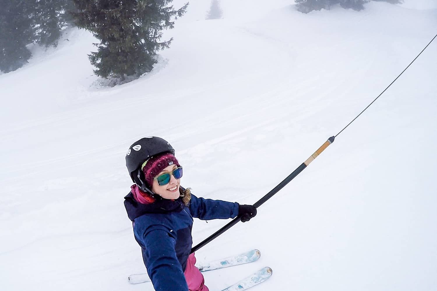 A woman dressed in blue and pink ski clothing glides up a small snowy hill on a t-bar lift in a Salzburg ski resort in Austria