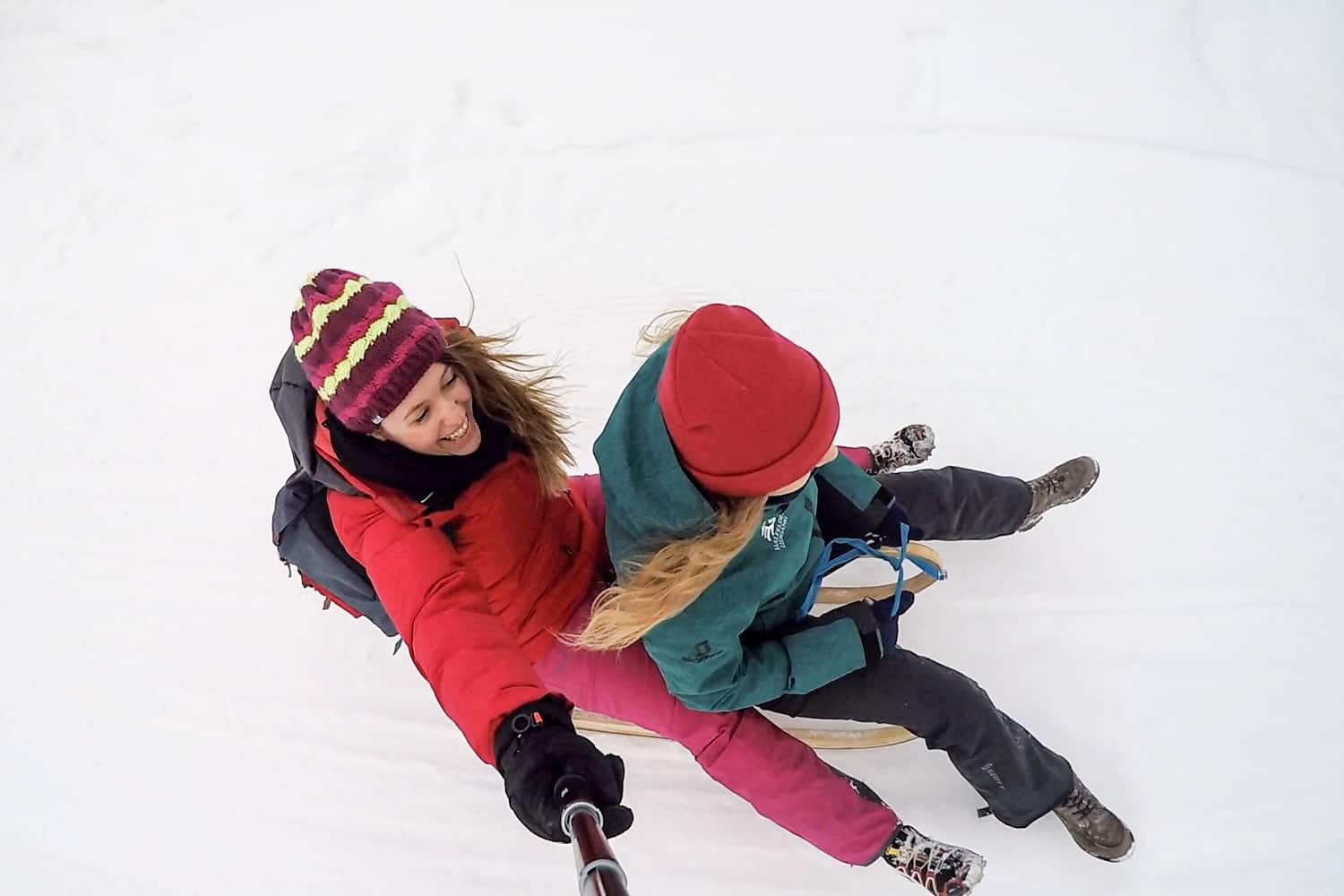 Two women in bright coloured ski clothing tobogganing on the Asitz Mountain snow track in Salzburg, Austria