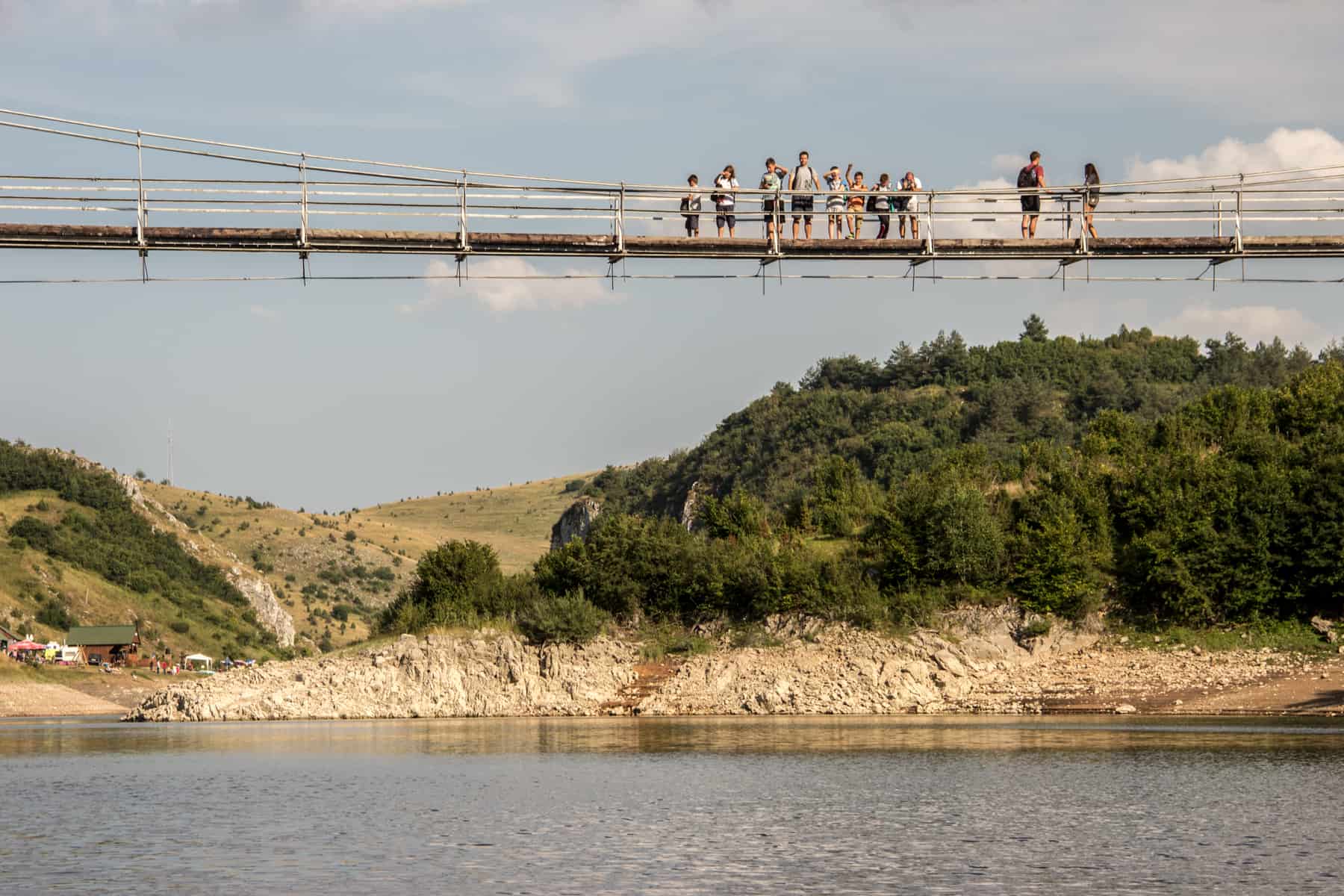 People standing in a line on a hanging bridge over a gorge backed by forest. 