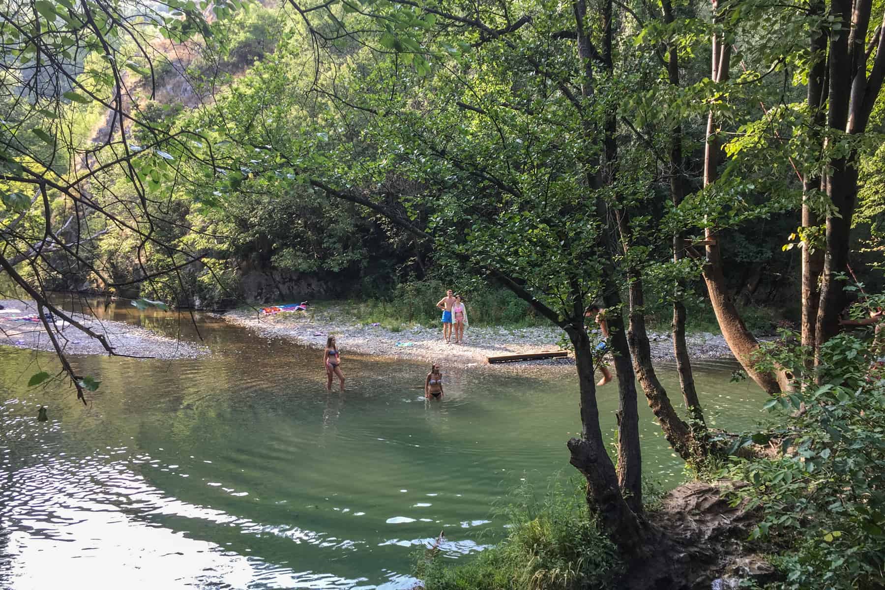 People wading through a shallow river in a forested gorge in Serbia. 