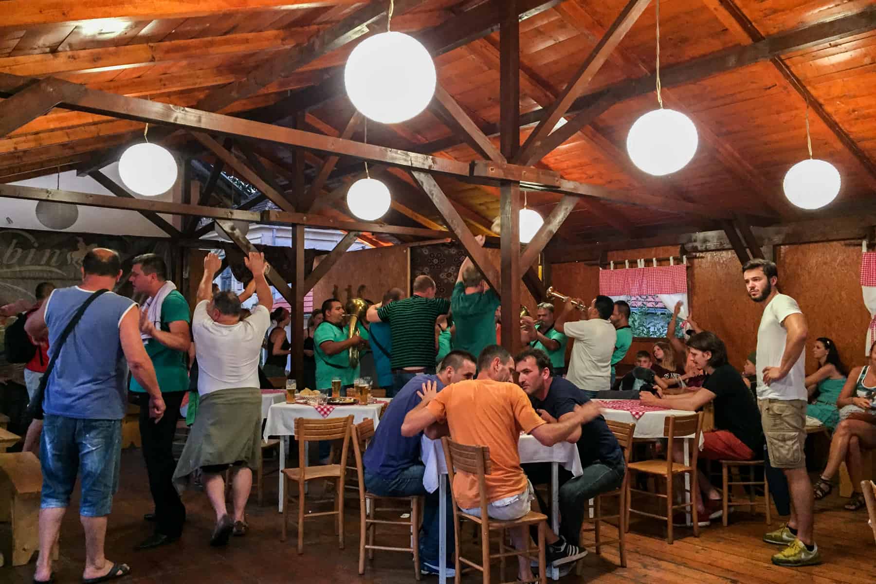 Inside a wooden building, trumpet players in green t-shirts play to the crowd, some of whom are dancing. 