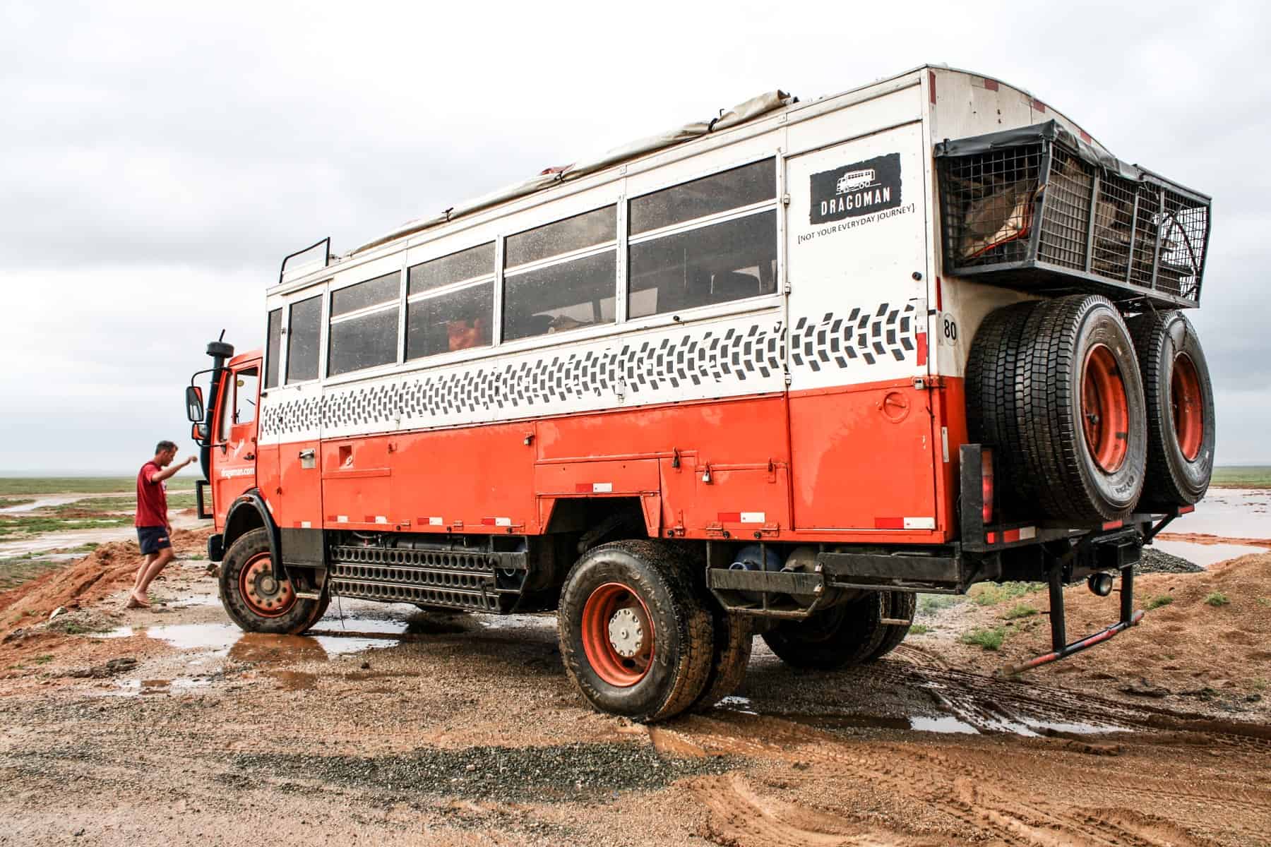 The orange and white overlanding truck used to travel to Mongolia and its rural landscape like the muddy one shown