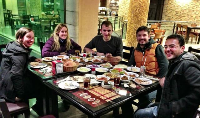 Five people sit around a table sharing food in a restaurant in Hebron