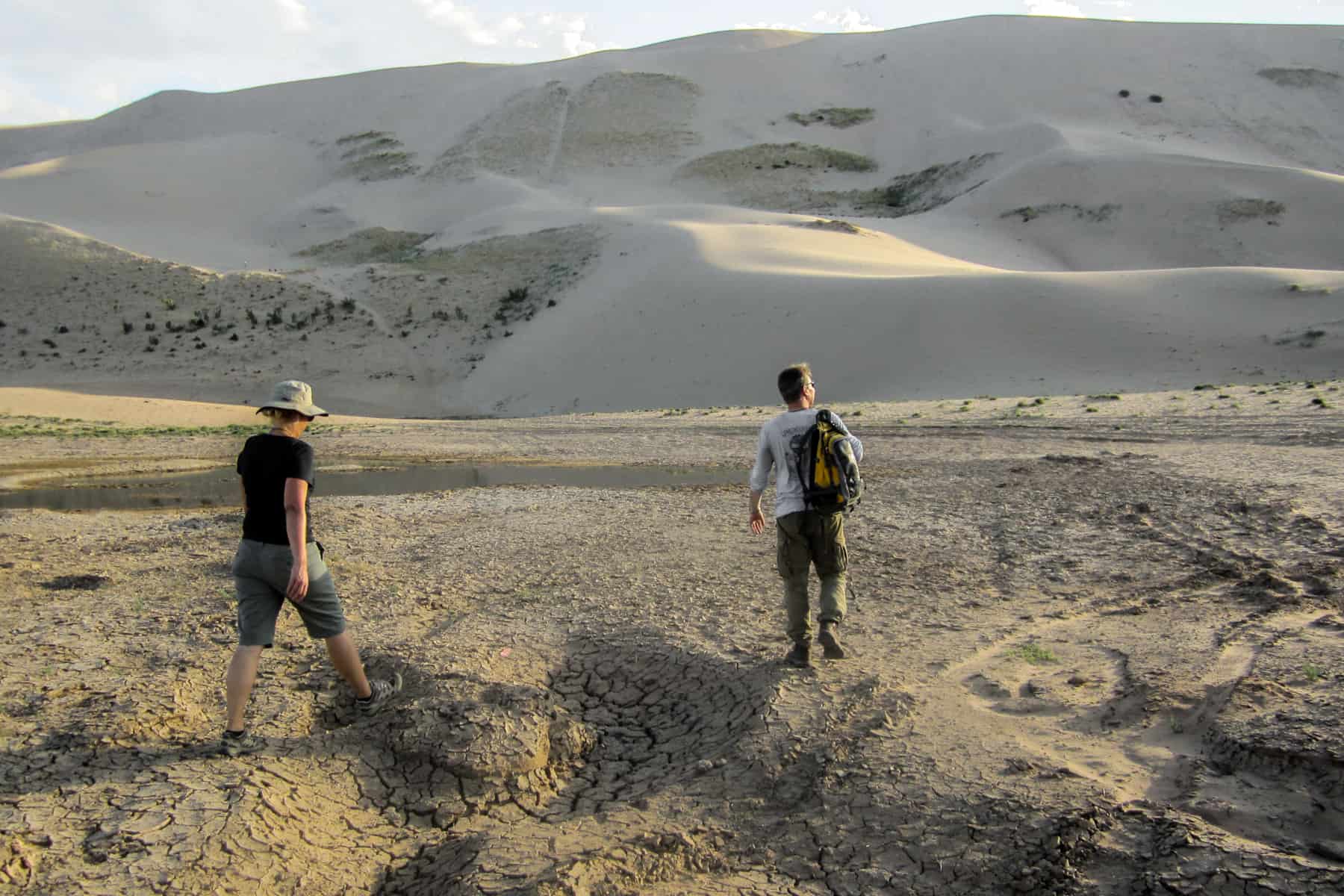 A man and woman walk through the Gobi Desert Mongolia towards the Khongoryn Els Sand Dunes in the distance