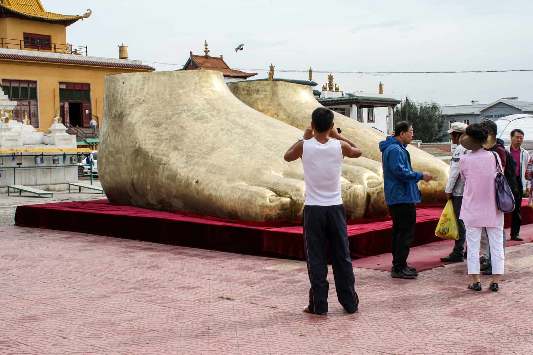 Three people photographing a pair of giant Golden statue feet outside the Gandan Monastery Ulaanbaatar Mongolia