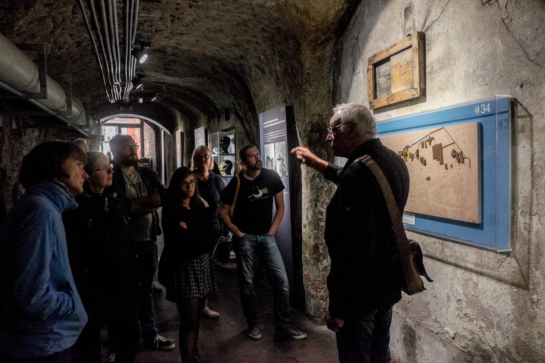 A male tour guide leads a small group in a narrow alley of the art bunker in Nuremberg, with the entrance door to the street in the background