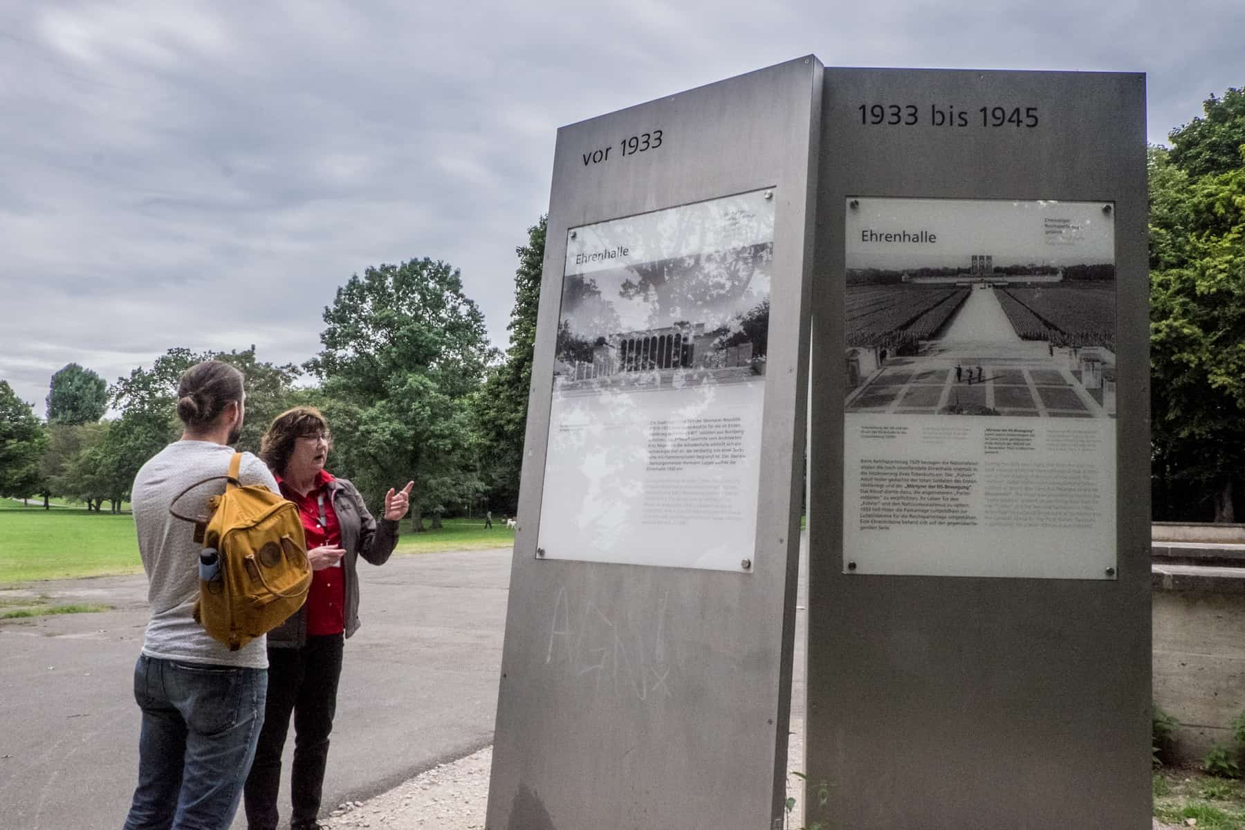 A male traveller with a yellow backback listens to a female guide at two information boards located at one of the former Nazi Party Rally Ground sites in Nuremberg, Germany