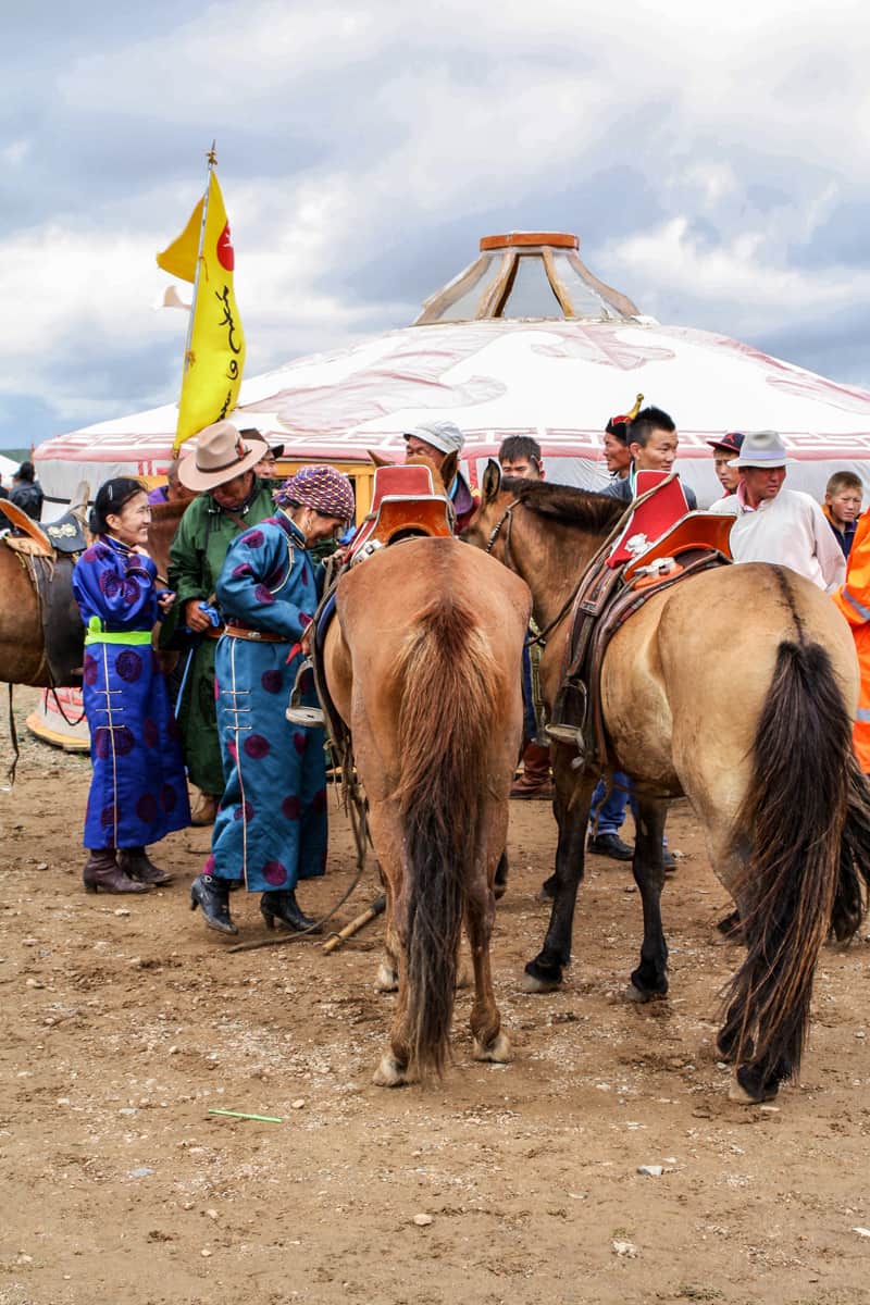 Mongoles con vestimenta local se reunieron afuera de un ger blanco con sus caballos en el Festival Nadaam en Mongolia