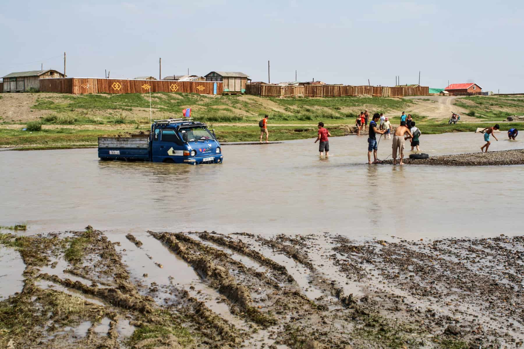 A blue truck is stuck in a pool of water in Mongolia as a group of people try to help