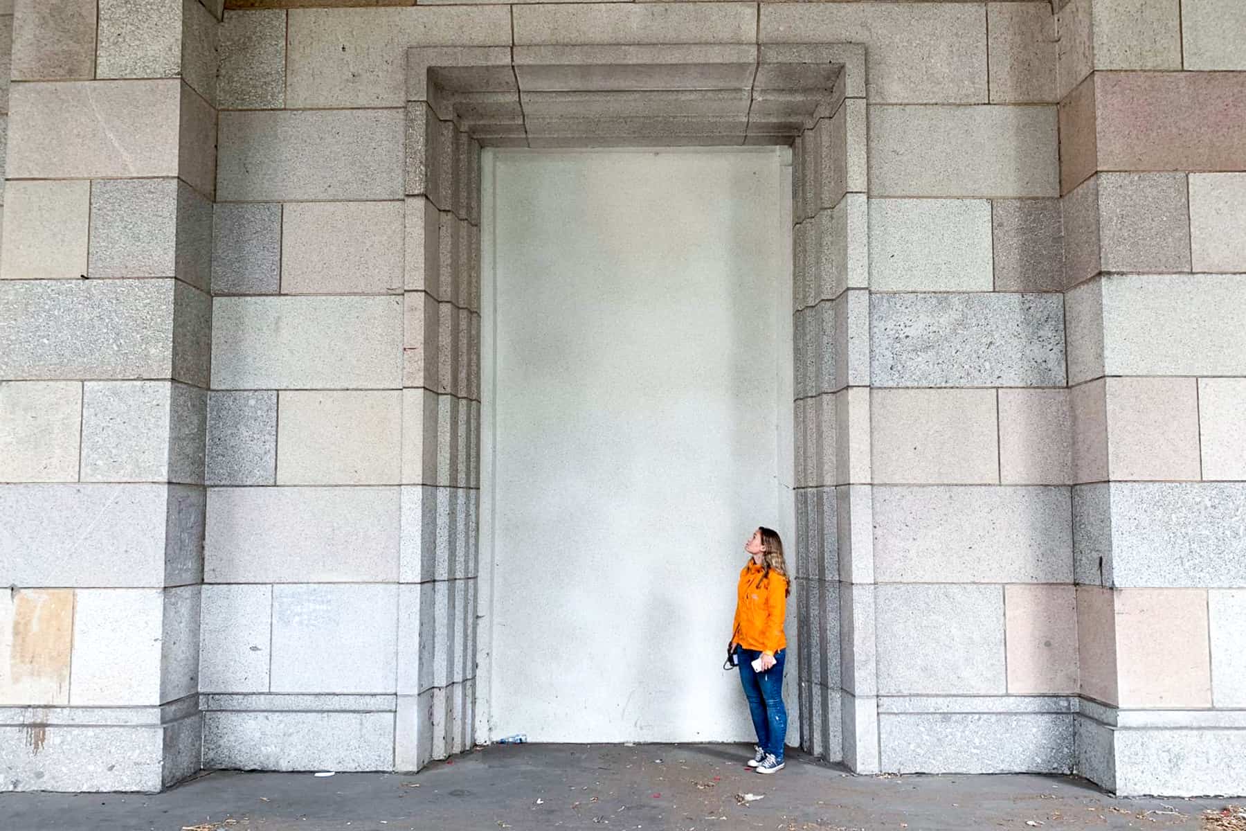 A woman in an orange jacket looks tiny in comparison the enormous marble stone doorway at the former Nazi Party Rally Grounds site of the Congress Hall in Nuremberg