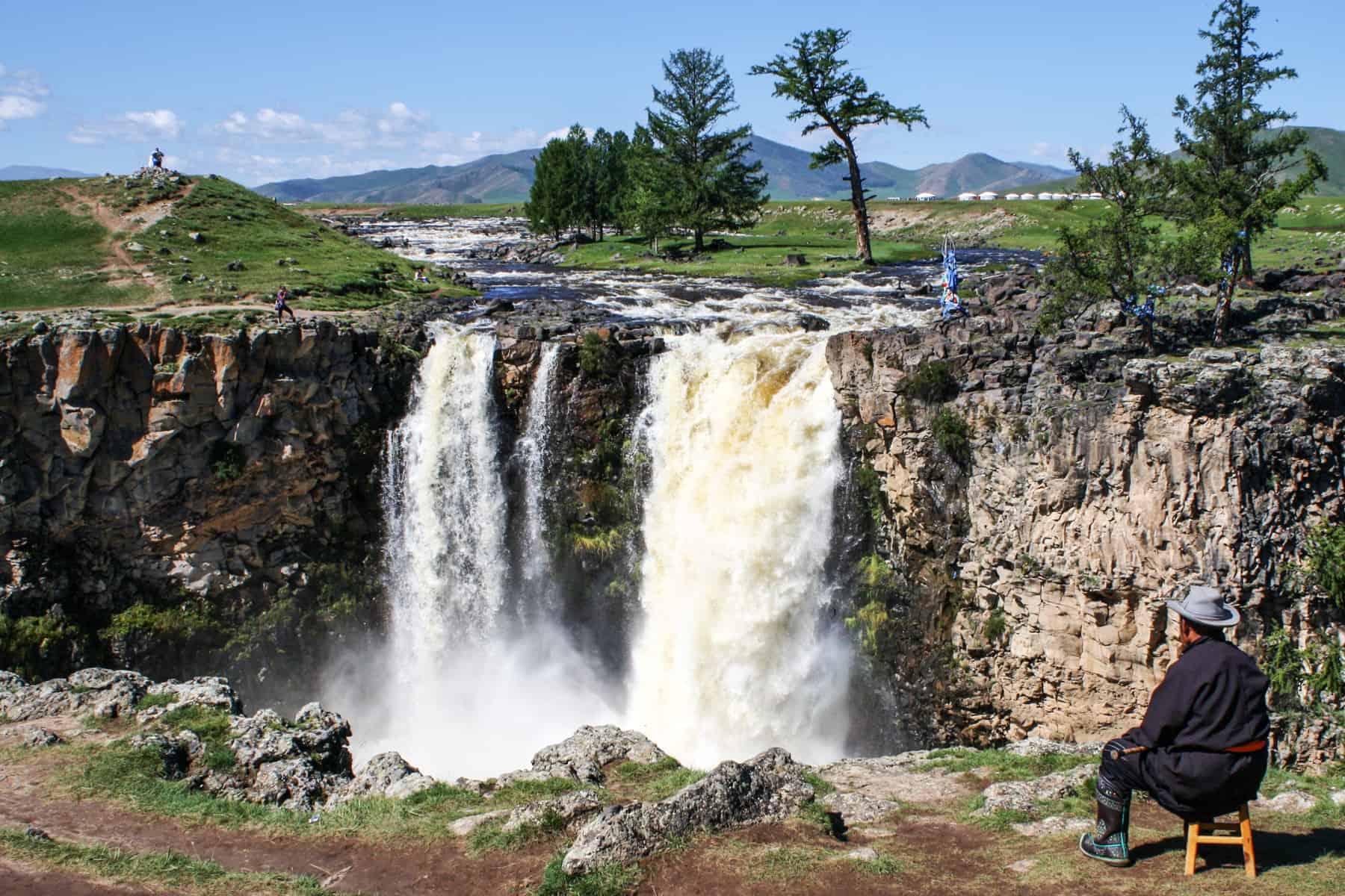 A Mongolian man sits in a chair peacefully enjoying the backdrop of the Orkhon Valley Waterfalls in Mongolia