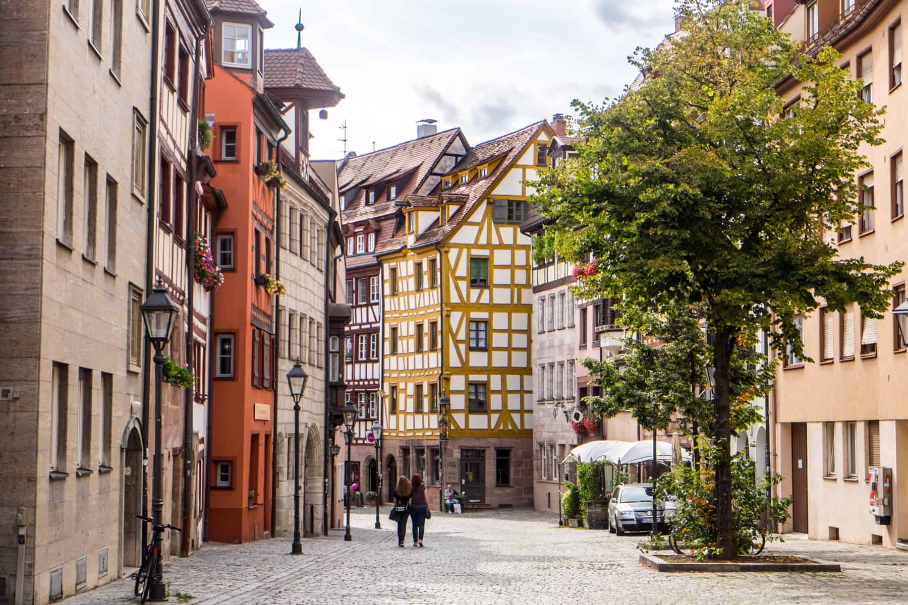 Two people walking amongst cream, orange, yellow and pink hued houses on a cobblestone street of Nuremberg Old Town