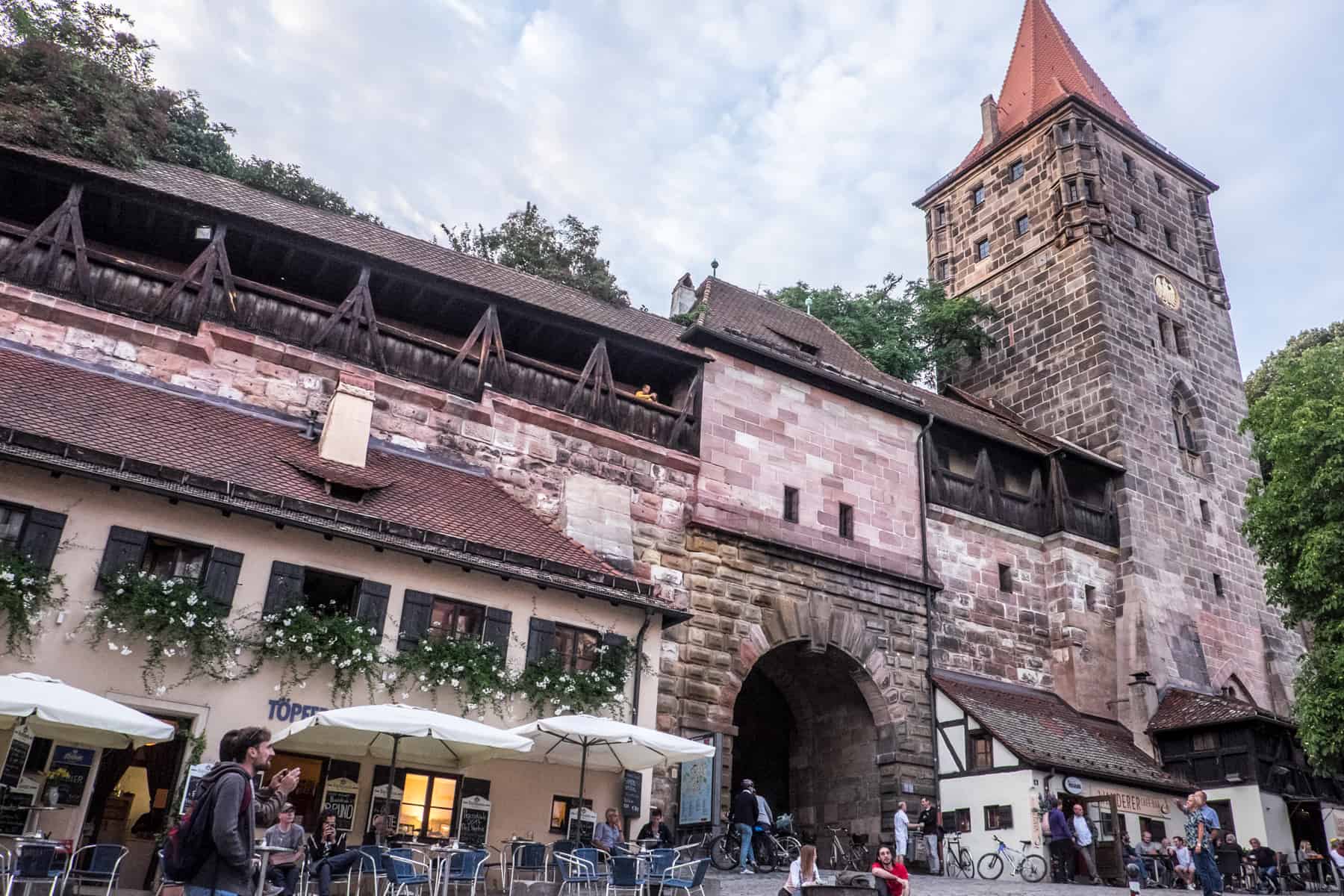View of Nuremberg Castle entrance marked by an arched tunnel and a single tower old town, with people gathering outside at one of the ground-level bars