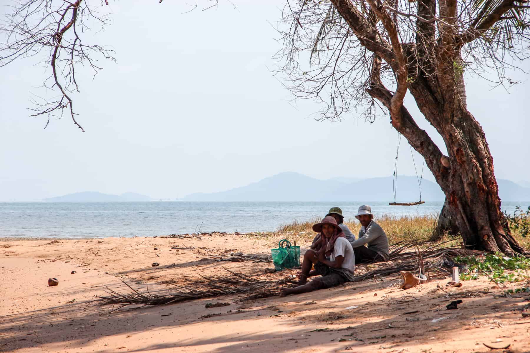 Three local fisherman take shade under a tree on the coastline of Rabbit Island