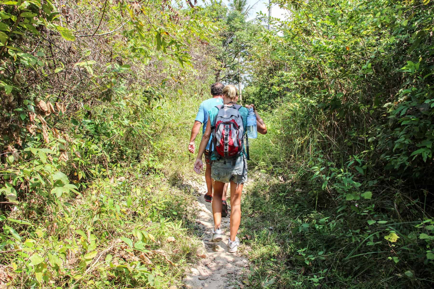 A man leads a woman through a narrow walking trail in dense forest