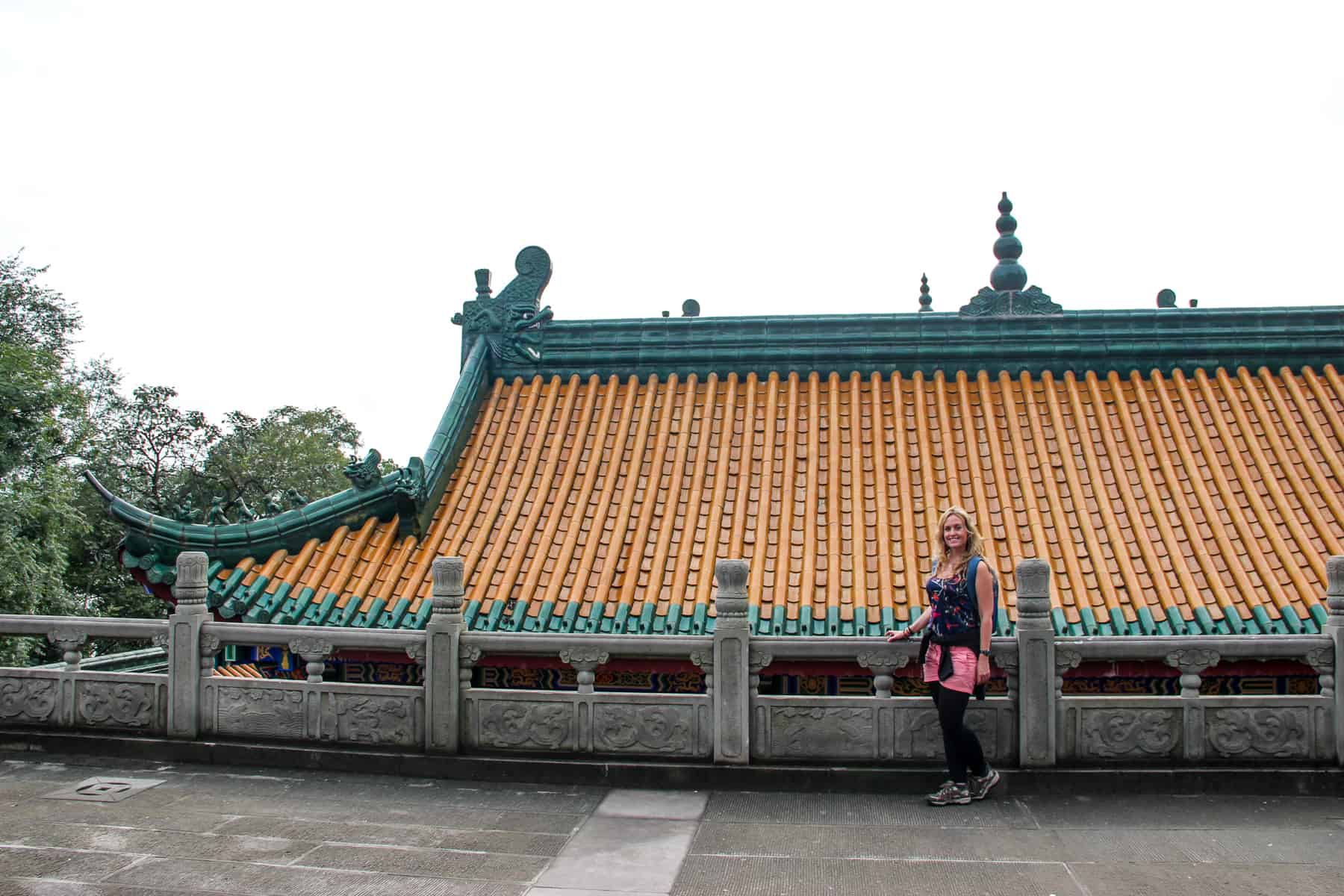 A woman stands in front of a golden upturned boat-shaped roof on a pagada in Fengdu Ghost city.