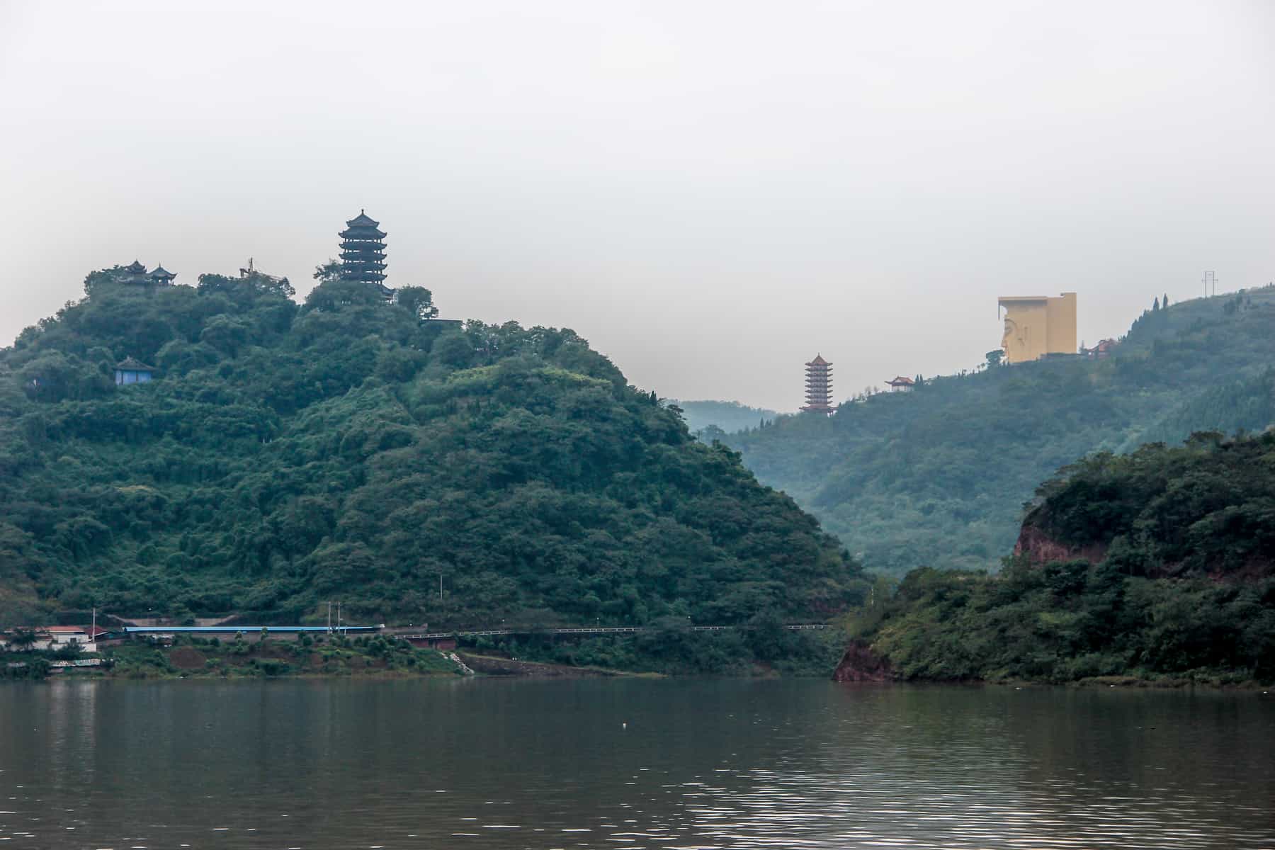 A pagoda tops a mountain on the left side and a golden face sits on top of the round hand mountain, as the Yangtze River flows between them