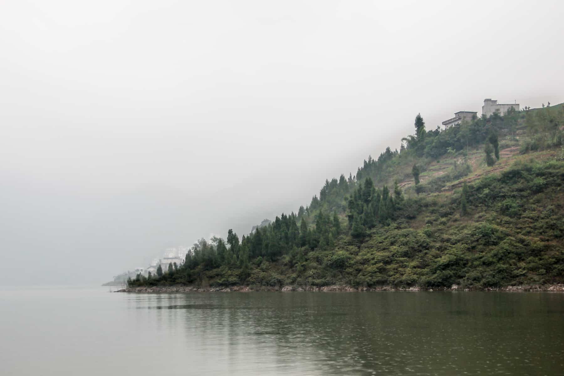 The end of a house-topped, tiny island sits pointedly in the Yangtze River, shrouded in fog