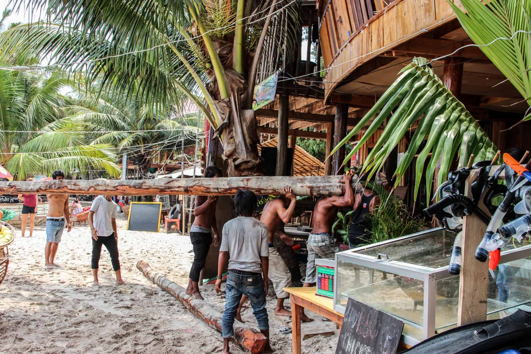 A group of Cambodian men working. on Koh Rong island carry a large tree log on their shoulders as part of beach hut building work