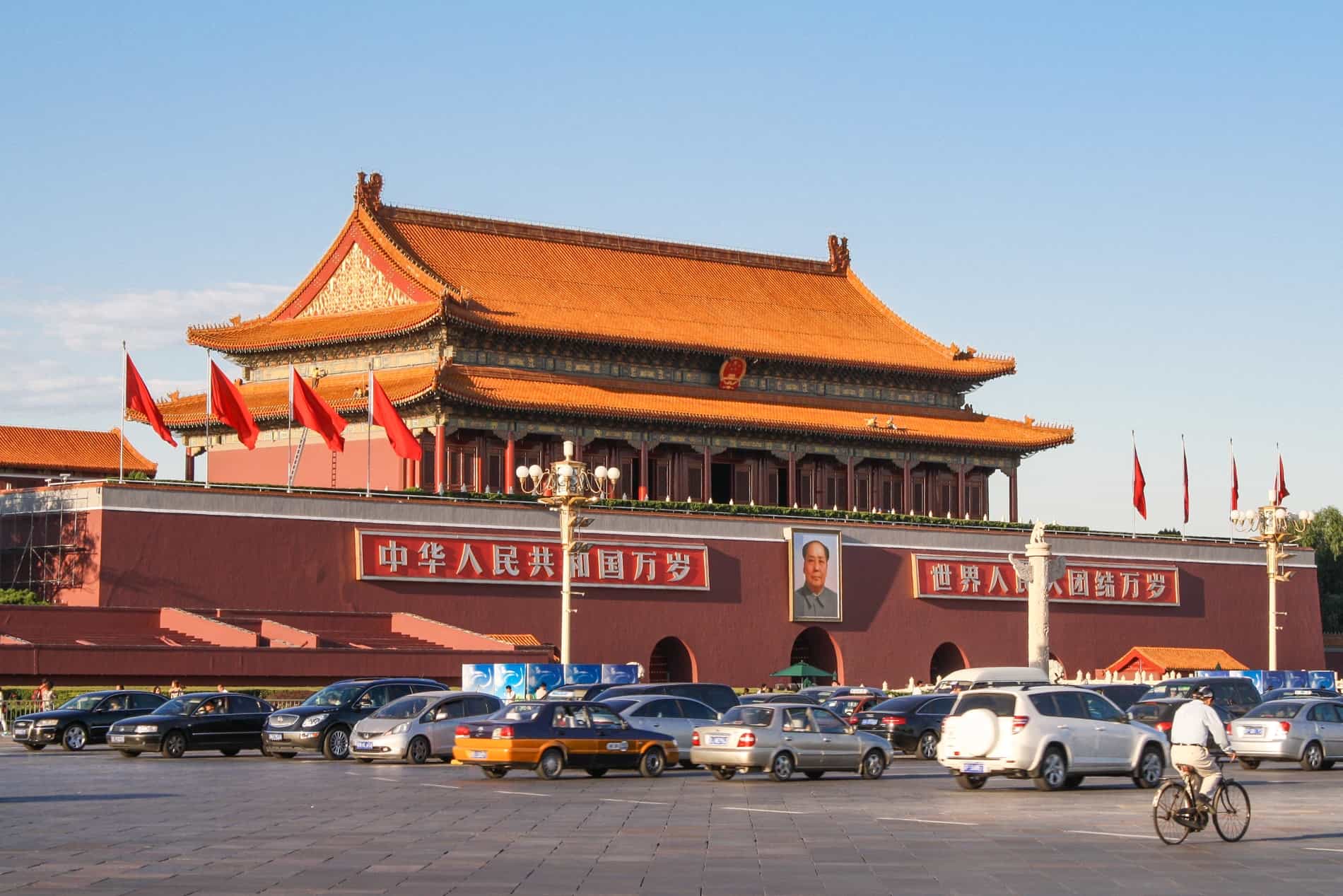 A two-tiered pagoda atop a red building with two panels of chinese characters and a portrait of Chairman Mao. 