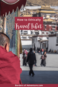 A Tibetan monk in a dark red robe looks towards a doorway entrance of the monastery in the background