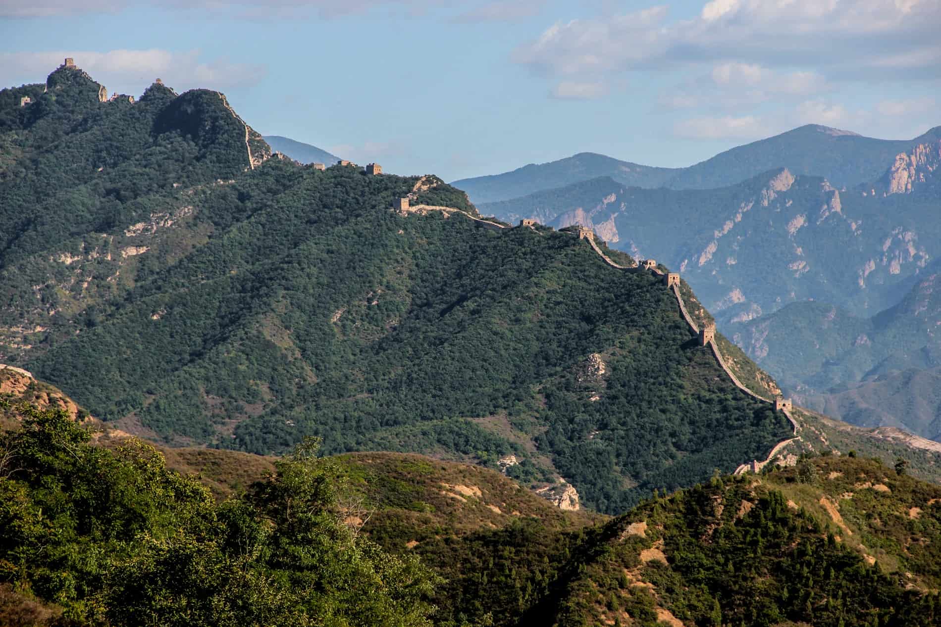 The Great Wall of China stretching along the jagged ridge of a forested mountain. 