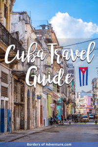 The multi-coloured crumbling buildings on a wide street in Havana, Cuba where a Cuban flag flies in the centre 