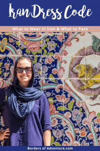 A woman wearing a blue robe and dark blue headscarf in Iran, standing in front of the multi-coloured mosaic wall of a palace