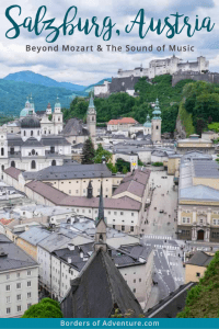 The green rooftops, church spires and quaint architecture of Salzburg, Austria, seen from an elevated viewpoint looking towards the hill with the mountains in the far background